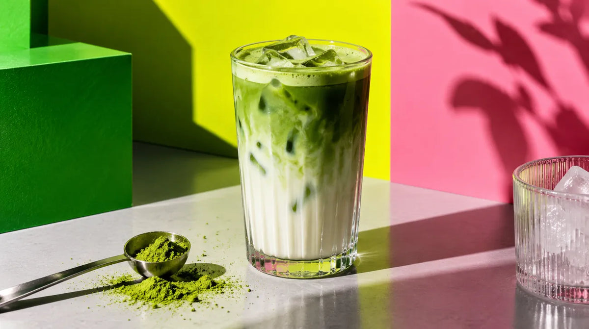 Matcha Latte mit Eis in einem hohen Glass und neben dran ein Matcha Messlöffel mit Matcha